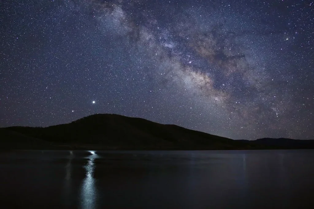 Saturn and Jupiter appear as two bright stars above a mountain ridge, reflecting brightly on the surface of a lake