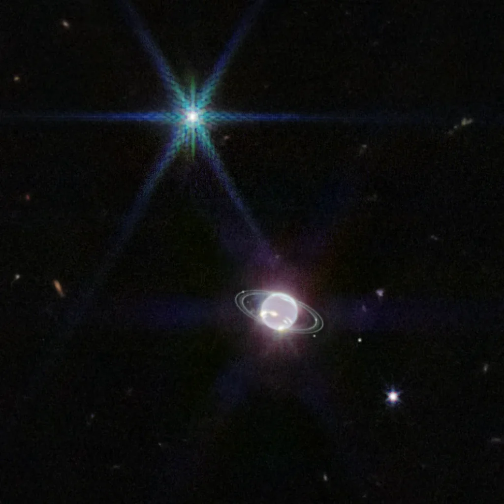 Image has a mostly dark background with one extremely bright point of light that dominates the upper left quadrant of the image and a glowing sphere towards the bottom middle of the image. The extremely bright point of light at the upper left of the image has 8 spikes pointing out from a center bright point like a compass. The glowing sphere, is mostly white, almost neon, with a few extremely bright patches of methane-ice clouds. The glowing sphere is accompanied by several narrow, faint rings and 6 tiny white dots, which are Neptune's moons. Splattered throughout the mostly black background are about 10 small, dim circles of distant galaxies.