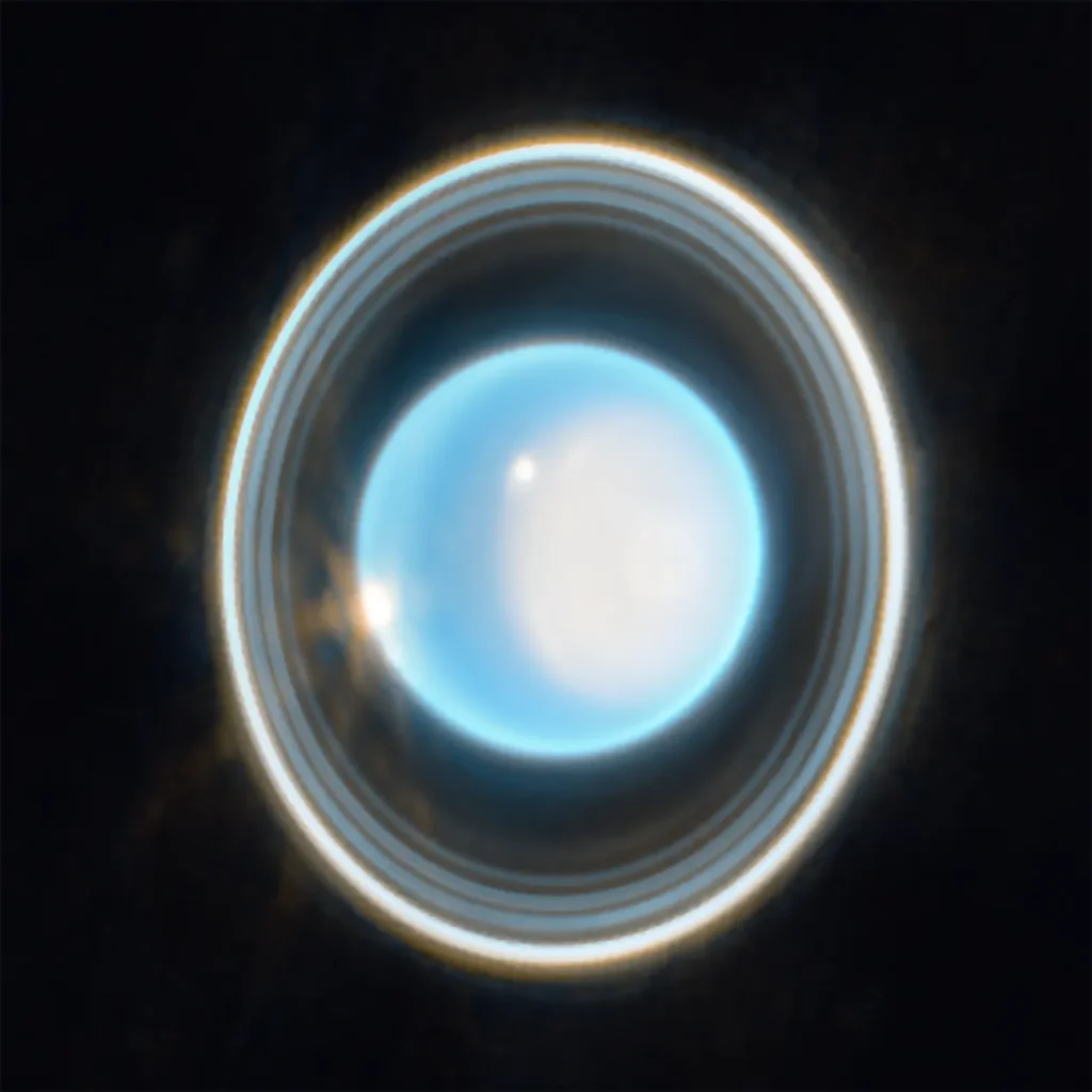 The planet Uranus on a black background. The planet appears light blue with a large, white patch on the right side. On the edge of that patch at the upper left is a bright white spot. Another white spot is located on the left side of the planet at the 9 o’clock position. Around the planet is a system of nested rings. The outermost ring is the brightest while the innermost ring is the faintest. Unlike Saturn’s horizontal rings, the rings of Uranus are vertical and so they appear to surround the planet.