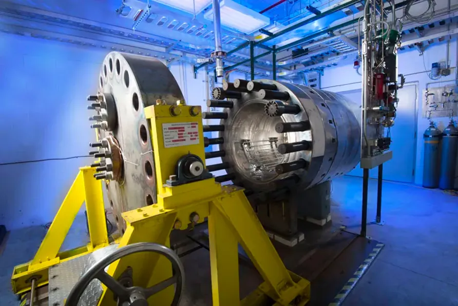 A large circular endcap with holes around its circumference next to a cylindrical test chamber with rods that fit into the holes on the endcap.