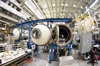 A laboratory containing several large tubes with protruding wires and tubes. The door to the tube in the center is open, showing the equipment inside the tube.
