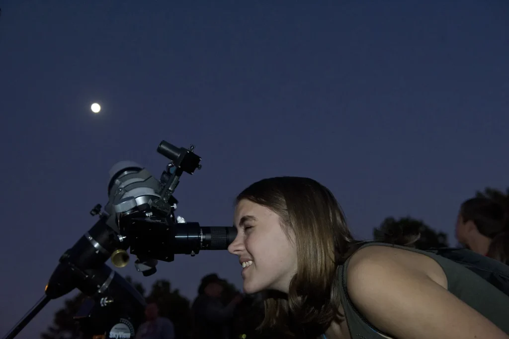 A woman peers at the Moon through a telescope.