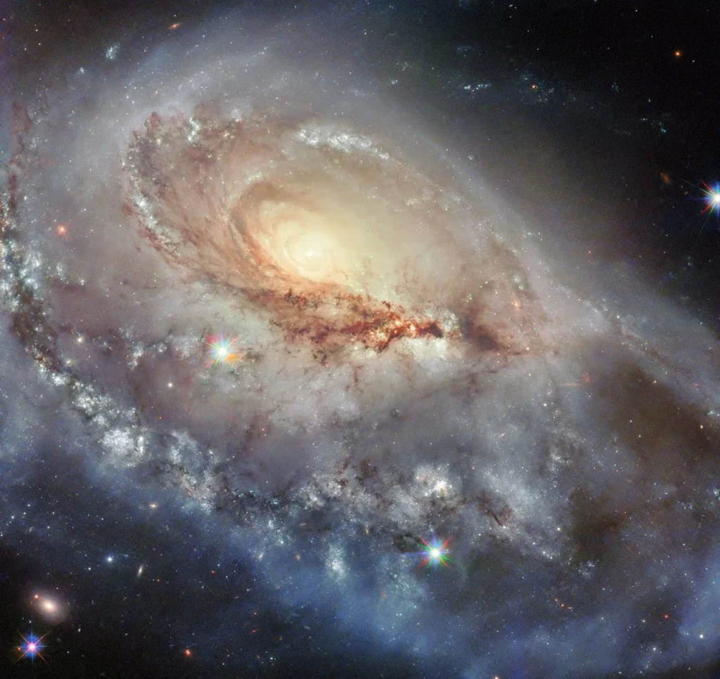 A spiral galaxy seen at a skewed angle. Its center is a bright spot radiating light. A thick, stormy disk of material surrounds this bright center, with swirling strands of dark dust and bright spots of star formation strewn through the disk. A large spiral arm extends from the disk toward the viewer. Some foreground stars are visible atop the galaxy.