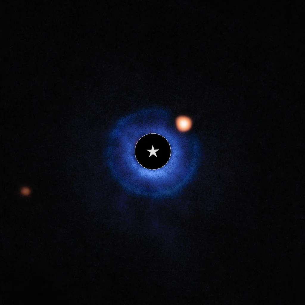 An image of a nearby star and its vicinity. The star itself has been blocked out and its bright light has been removed, appearing black. A dashed circle with a star symbol at the center of the image marks the star’s location. A fuzzy blue disk surrounds the star. An orange spot, near the star and inside this disk around 2 o’clock, is identified as a planet orbiting the star. A fainter orange spot at the lower left edge marks a distant star.