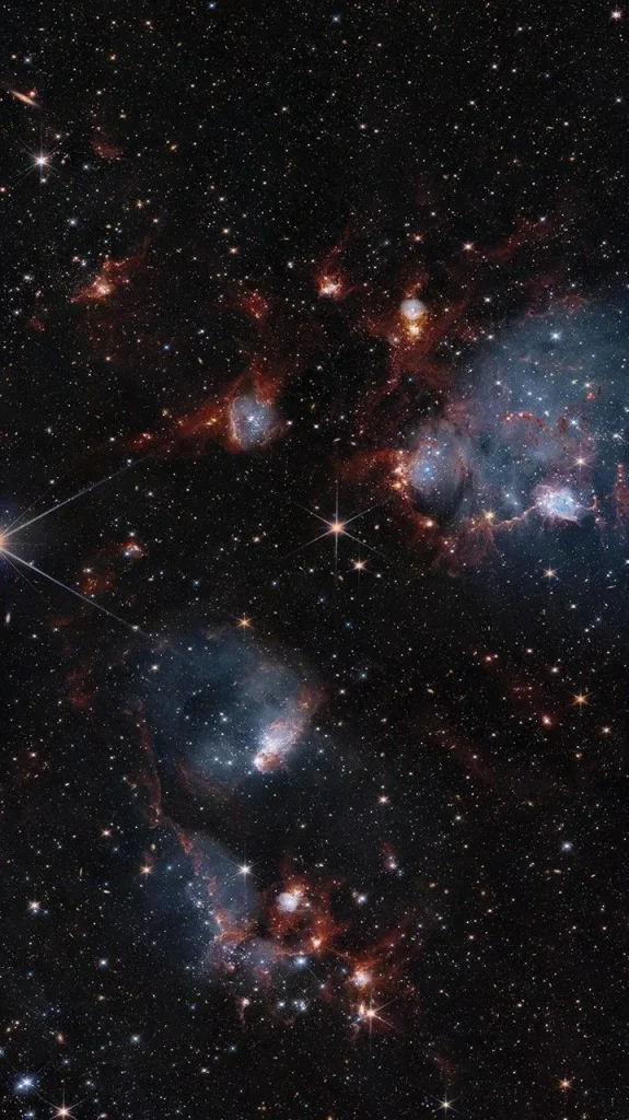Bluish clouds of gas are wound through with red-glowing lanes and filaments of dust.. The clouds contain cavities filled with stars and many more stars are visible in the background and scattered throughout the clouds. The clouds are concentrated in the upper right and the lower middle of the image. Tiny background galaxies are also sprinkled throughout the image.