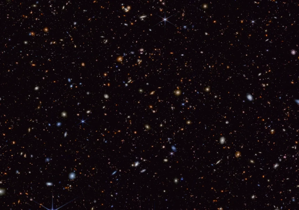 Webb Space telescope deep field image showing hundreds of objects of different colors, shapes, and sizes scattered across the black background of space.