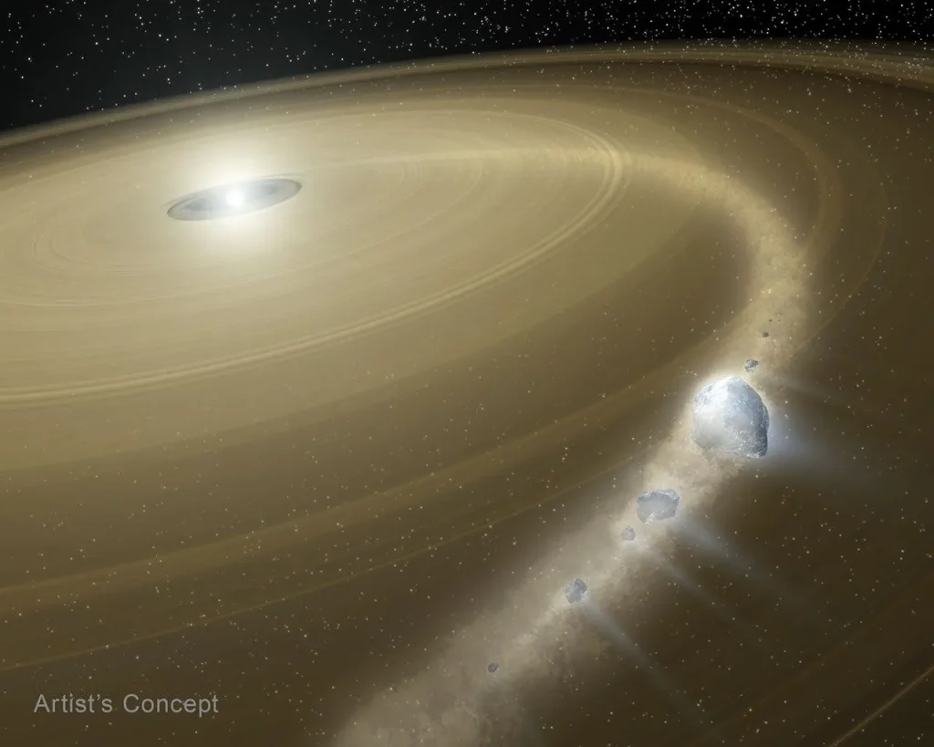 An illustration showing a glowing white object in the upper left corner. This object is encircled by hundreds of thin, concentric, pale-yellow rings on an angle from bottom left to top right. The rings are palest closest to the central, glowing white object. A curving trail of gray, rock-like fragments marches across the right side, through the thin rings and joins the rings at far right. The eight largest fragments of varying sizes appear in the foreground. These objects have white, comet-like tails streaking away from the glowing white object in the rings’ center. The curving trail of fragments bends toward the glowing white object. At the bottom left corner is the label Artist’s Concept.