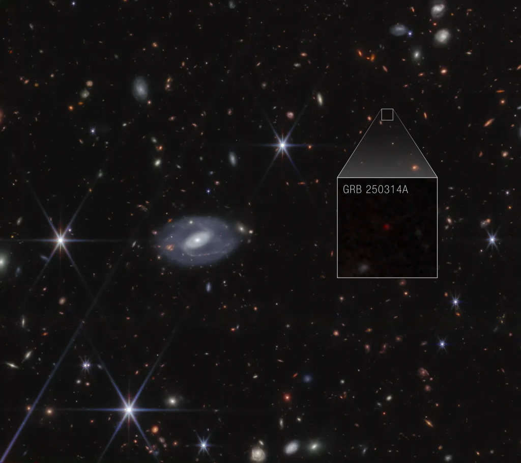 Webb image shows hundreds of galaxies of all shapes and sizes against the black background of space. Toward the center-right is a large box that zooms in to show a faint red dot with the label GRB 250314A.