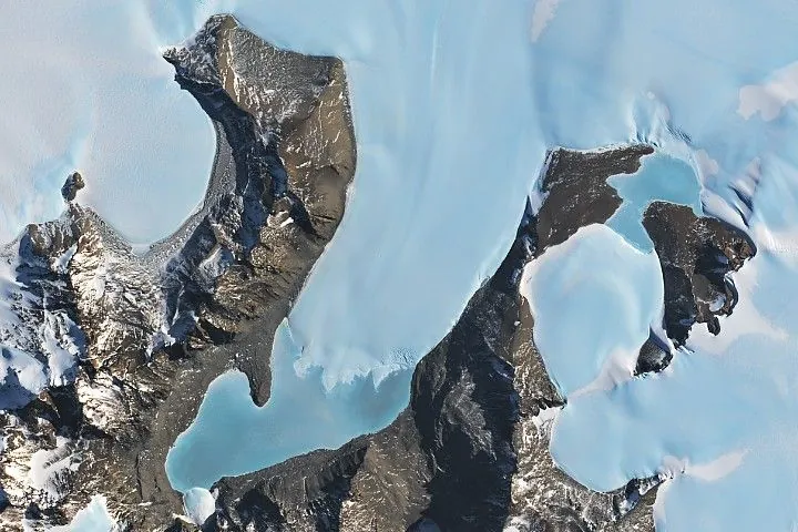 The image is centered on Anuchin and Ober-See glaciers in Antarctica. They appear as bright white patches separated by brown rocky ridges. Both glaciers have ice-covered meltwater lakes draining from their termini. Lake Unter-See is the larger of the two lakes.