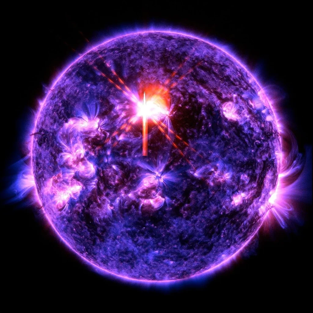 The Sun against a black background. The Sun is colorized primarily in blue, with some brighter purple areas scattered across the star showing higher activity areas. Toward the upper center of the star, there is a bright flash in white and red, which looks like an X -- the solar flare.