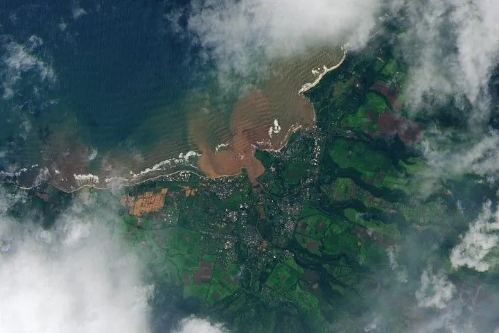 The same area, with brown floodwater pooling across farmland between Mokuleia and Waialua, with a red-brown plume spreading into the coastal ocean.