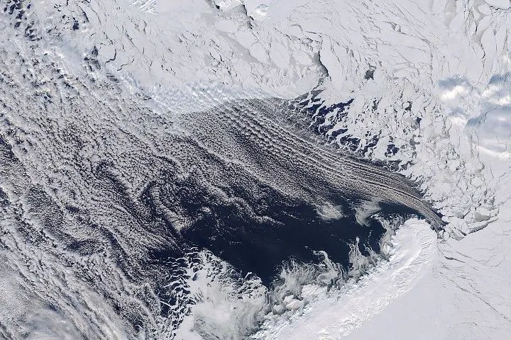 Dark open water lies south of thin, broken up sea ice near Franz Josef Land, with a thin layer of clouds covering part of the scene.