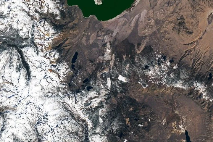 A string of small, partially snow-covered volcanic craters runs north-south between Mono Lake and Mammoth Mountain. Snowy mountains fill the left side of the image.