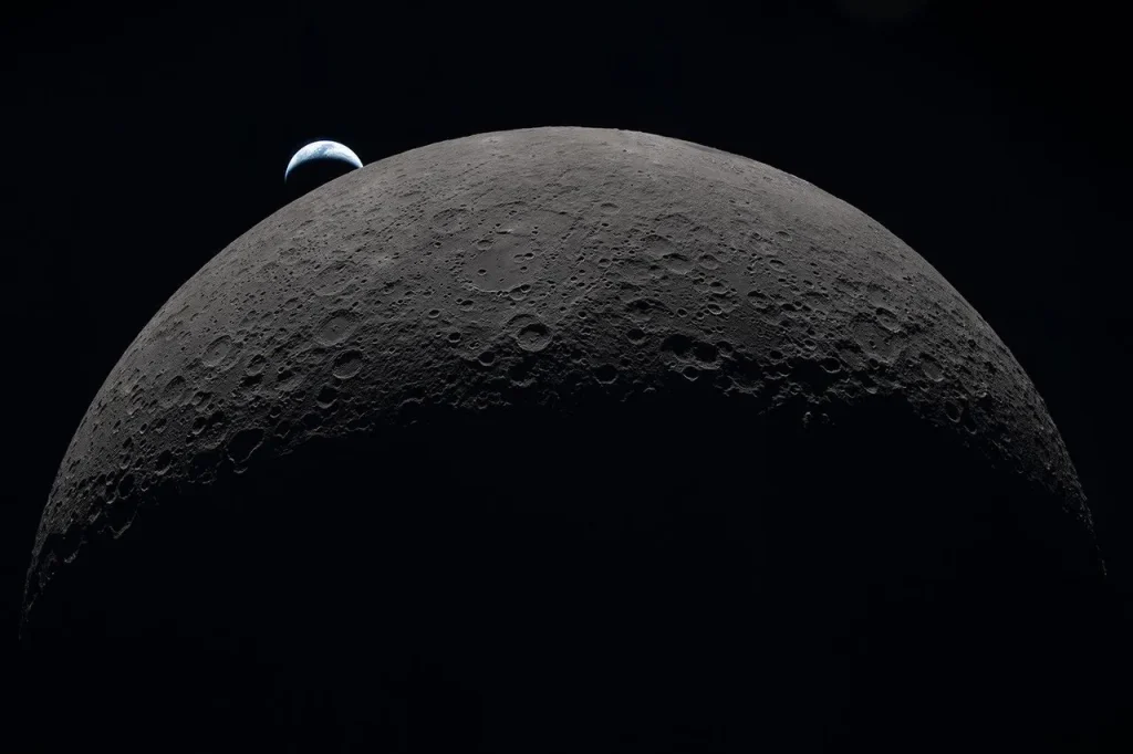 The gray-brown, heavily cratered Moon dominates the frame against black space, with a partially lit crescent Earth setting behind its upper-left edge.