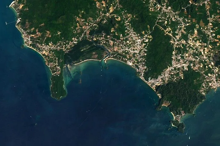 Alt text: Strips of sandy beach line the coast of Krabi Province, Thailand, separating blue ocean water from inland greenery and urban areas.