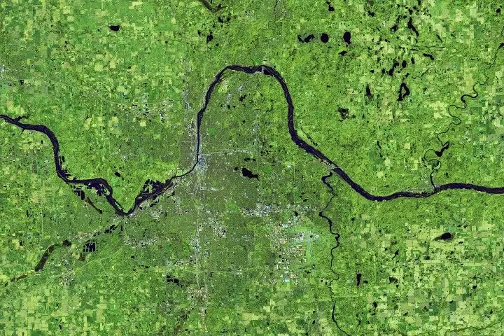 The Grand River in Michigan is wider than the previous year at the same time, swollen with floodwater. Water is dark blue, and vegetation appears in shades of green in this false-color image.