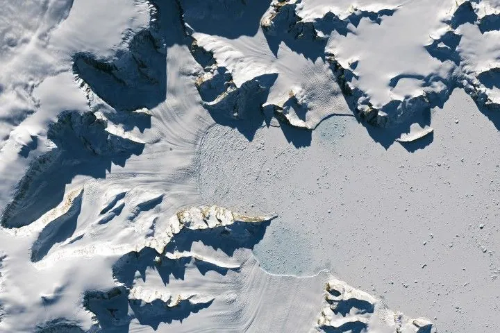 Glaciers flow from the left and bottom sides of the image, terminating much closer to the cliffs than in the previous image.