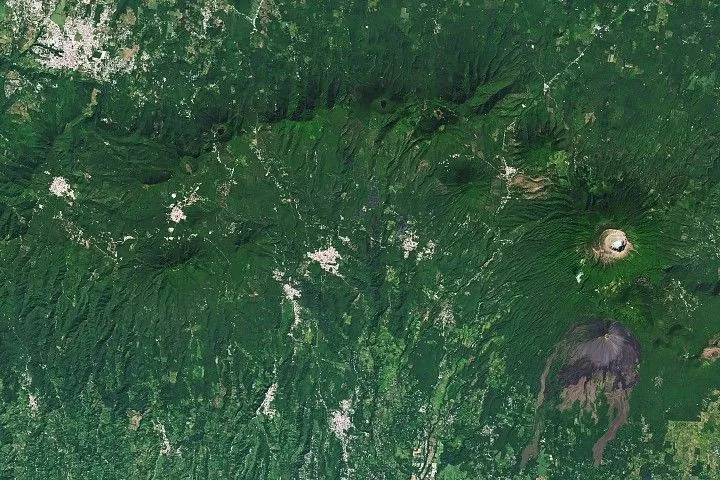 A chain of forested volcanic peaks arc across the image, with an area of dark lava flows in the lower right and the brighter urban area of Ahuachapán in the upper left.