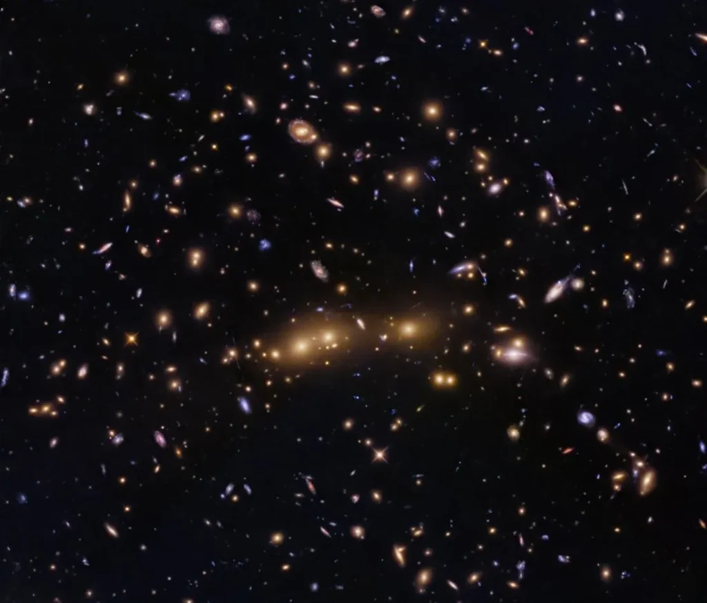 Several massive elliptical galaxies appear to sit in a nearly horizontal line across the center of the image. Numerous spiral, lenticular, and smaller elliptical galaxies dot the space surrounding the giant ellipticals.