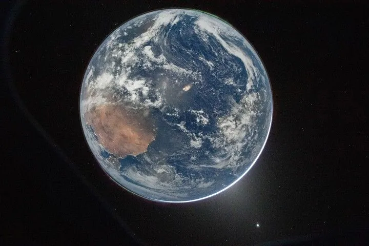 Earth’s full disk is seen through the window of a spacecraft. The glow of aurora, a sliver of the Sun, and fuzzy zodiacal light surround the planet, and city lights are visible on the continents.