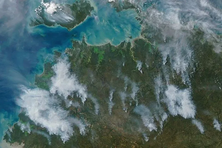 Several gray smoke plumes are visible drifting over a green landscape.