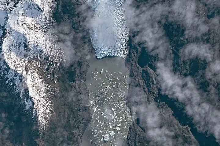 A top-down photo shows a detailed view of the leading edge of a glacier terminating in a lake. The glacial ice is heavily crevassed with intersecting linear features.