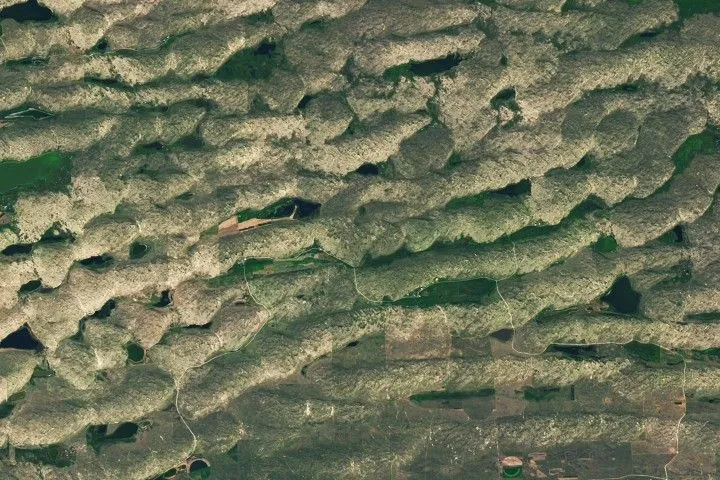 A series of tan parallel ridges runs from left to right, with green areas and small lakes filling the low-lying spaces in between.