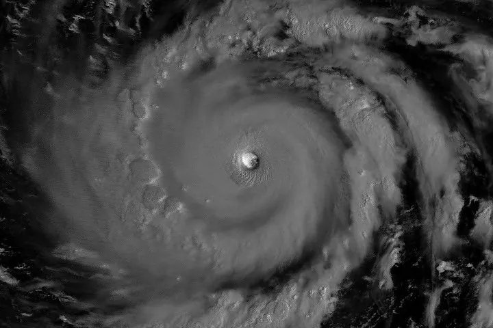 The eyewall of a super typhoon is partially illuminated by moonlight in a nighttime satellite image.