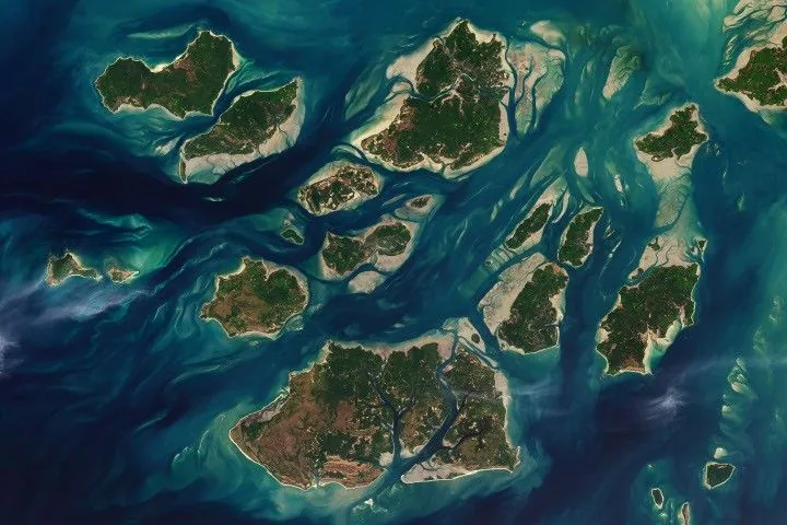 A satellite image shows a cluster of green islands surrounded by beige sand flats and networks of channels full of dark blue water.
