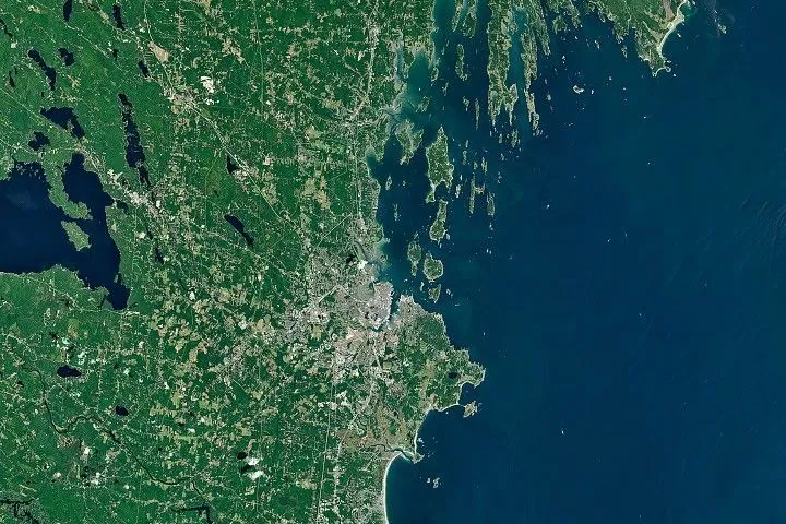 A satellite image of the Maine coastline highlights smooth, sandy beaches near Saco Bay on the left and the rocky, jagged coastal features near Casco Bay on the right.