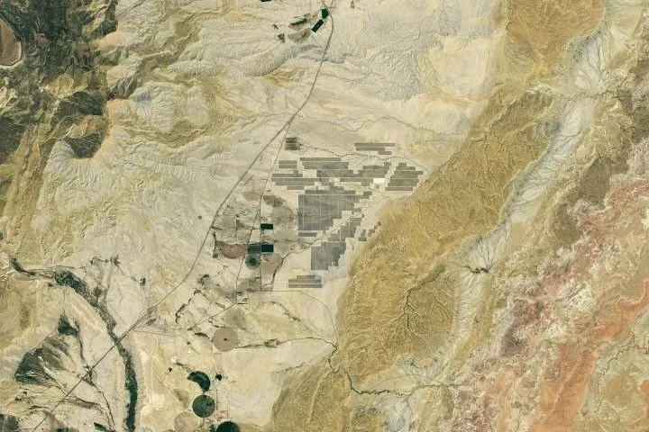 Grid-like arrays of solar panels cover parts of a valley floor in a brown, dry-looking area of Utah.