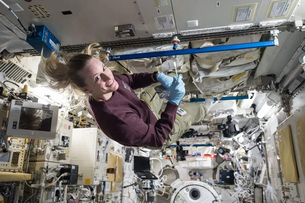 Astronaut conducts scientific work aboard the International Space Station, floating in microgravity surrounded by equipment and research tools.