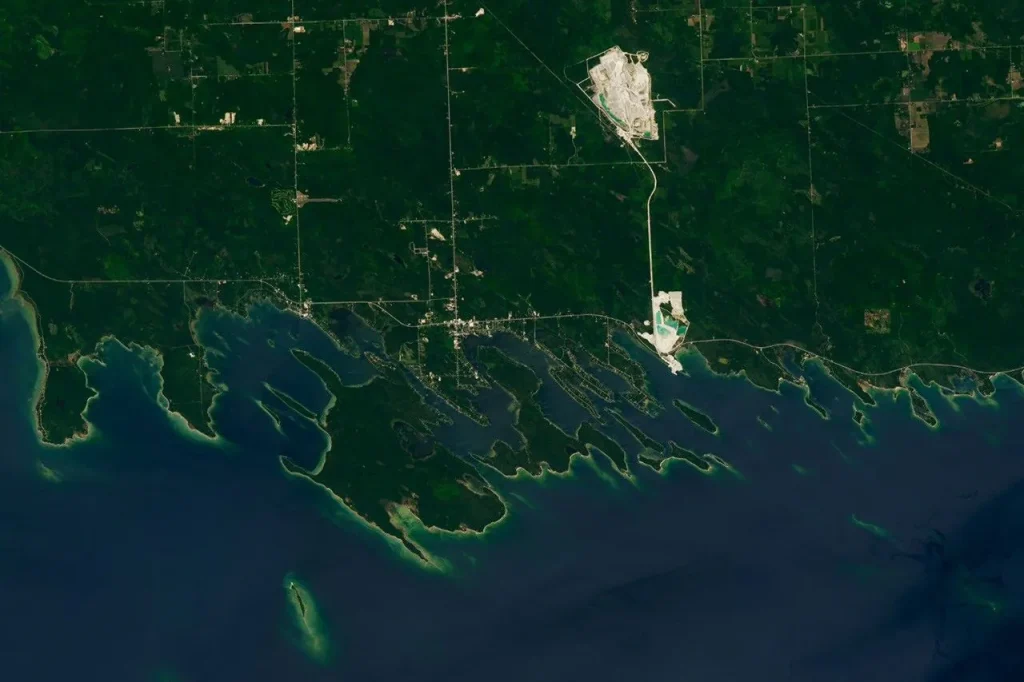 A portion of the Upper Peninsula of Michigan runs across the top of the image. It is mostly green, with some roads and two bright rock quarries visible. Numerous islands near the shore have elongated shapes and are oriented at a diagonal.