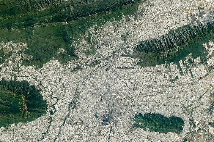 The light-colored urban development of Monterrey, Mexico, fills most of the top half of the photo, and green parallel mountain ridges arc across the bottom of the frame.