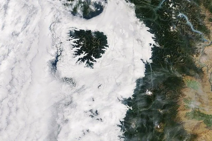Low-lying clouds cover western Washington and Oregon between the Pacific coast and the foothills of the Cascade Range. Parts of the Olympic Mountains and Oregon Coast Range are visible above the clouds.